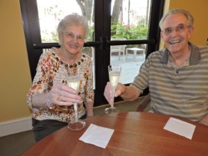 Smiling man and woman raising glasses of champagne. When is the Best Time to Move to a CCRC?