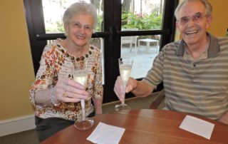 Smiling man and woman raising glasses of champagne. When is the Best Time to Move to a CCRC?